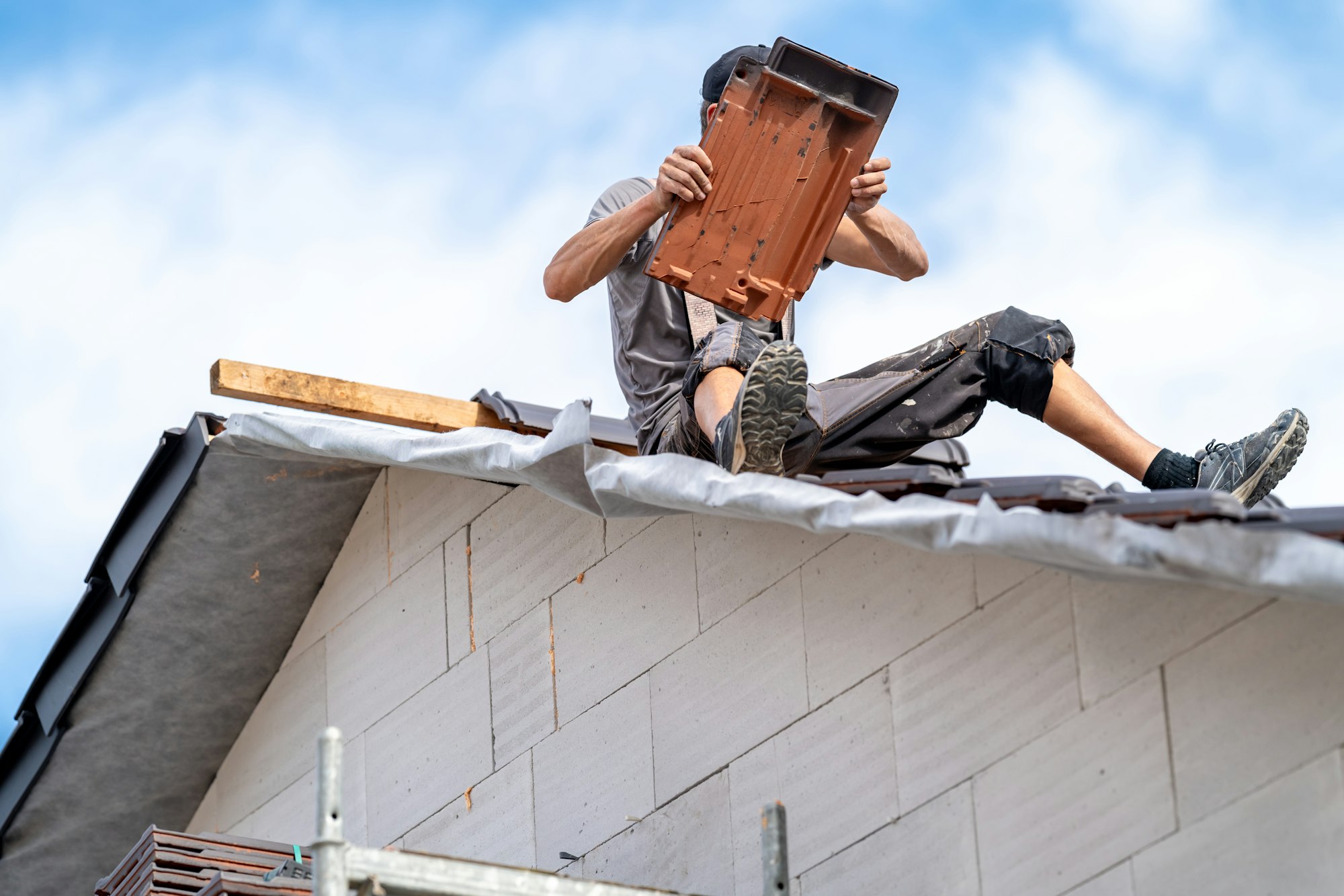 roofer with ceramic tile in hand on roof of house